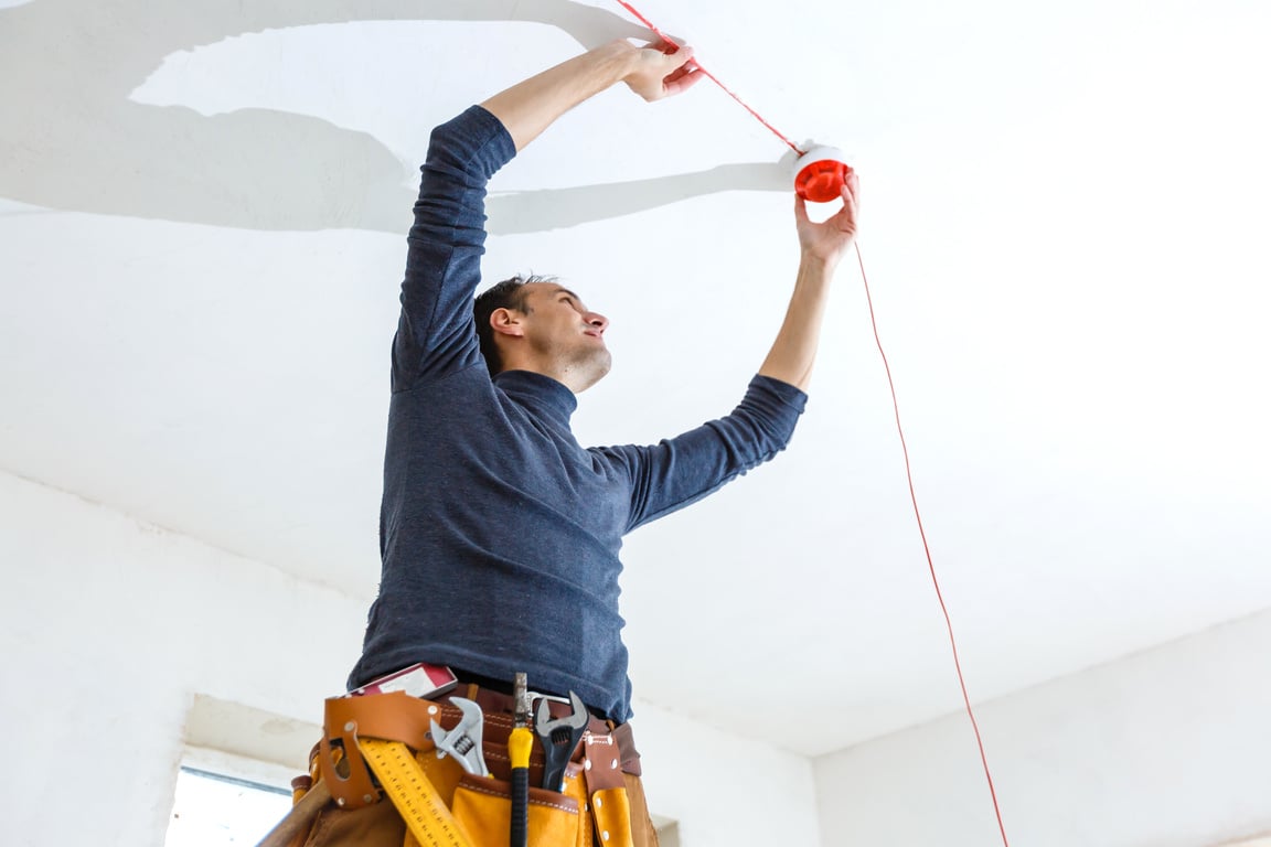 Electrician installing fire alarm system indoors